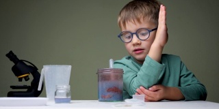 选择学校。戴眼镜的男孩在做实验。年轻科学家为实验配制液体。学龄前儿童室内玩耍。家实验室背景。学习有兴趣