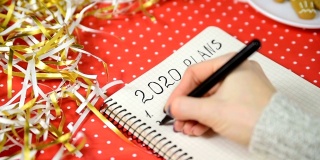 女性在笔记本上写下2020计划。红色背景和金属丝。年新概念