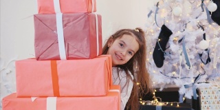 可爱的小女孩为她的朋友和家人准备了圣诞礼物，她从一堆红色礼品盒后面偷看出来。