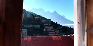 镜头移向茶馆窗口，用男手打开。然后，纳姆切巴扎(Namche Bazaar)尼泊尔小镇的景观在一扇窗户后展现出来。住在珠穆朗玛峰基地营地徒步旅行POV视频小屋。