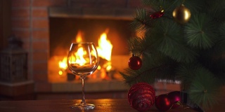 桌子上有一杯葡萄酒和一棵圣诞树。背景是一个燃烧的壁炉。新年假期酗酒。酒精饮料的概念。火的背景。独自喝。餐厅的饮料。