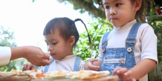 可爱饥饿的小女孩喜欢在后院吃妈妈自制的披萨。小女孩和家人在户外吃午饭。