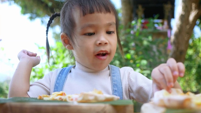 可爱饥饿的小女孩喜欢在后院吃自制的披萨。小女孩和家人在户外吃午饭。有选择性的重点。