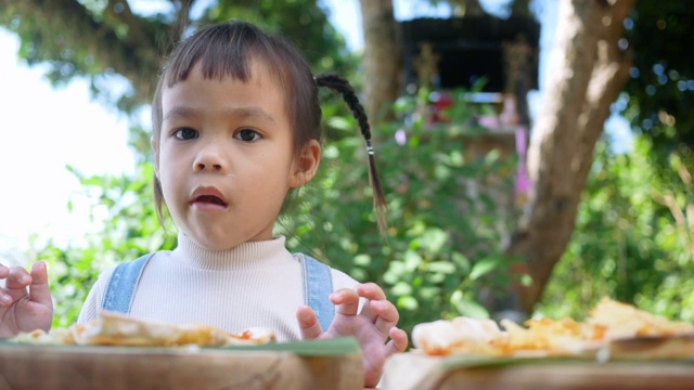 可爱饥饿的小女孩喜欢在后院吃自制的披萨。小女孩和家人在户外吃午饭。有选择性的重点。