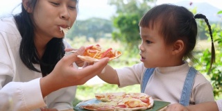 可爱饥饿的小女孩喜欢在后院吃妈妈自制的披萨。小女孩和家人在户外吃午饭。