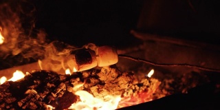 近距离拍摄的女孩烤棉花糖在一个舒适的篝火上使用棍棒。棉花糖着火了，她把它们吹灭了。用RED摄像机拍摄，慢动作。
