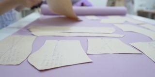 一位年轻的女裁缝时装设计师在一种淡紫色的织物上摆出图案来创造一件连衣裙。