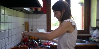 年轻女子烹饪酱汁，在厨房使用数码平板电脑
