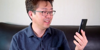 亚洲中年男子有一个愉快的视频通话使用智能手机。