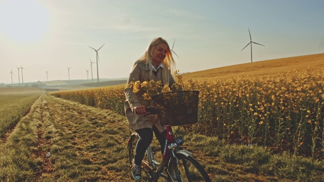 沿着油菜籽田骑自行车的妇女，远处有风力涡轮机