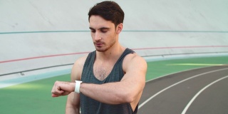 一名跑步者在体育场看智能手表。年轻慢跑者检查结果