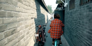 中国北京，在胡同里骑自行车的女人。