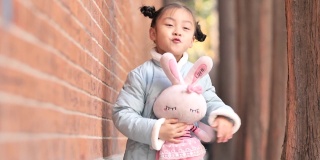 快乐的中国女孩穿着蓝色的新年衣服，抱着她最喜欢的兔子玩具在户外跳舞，4-5岁，非常可爱，4k视频，慢镜头。