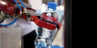 近景为红色机器人手拿一瓶水，背景模糊，人工智能概念。媒体。自动化工业机械设备