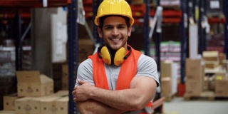 一名在配送仓库工作的拉丁美洲男子双臂交叉，面带微笑地看着镜头