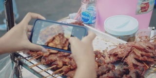年轻女性在街头美食中拍摄烤鸡和猪肉