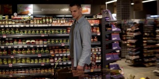 一名身穿蓝色衬衫的白人男子在一家超市的农产品部购买水果和蔬菜。拿起柚子，放进黑色的提篮里，再往前走。大杂货店