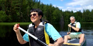 一对成年夫妇在芬兰的森林湖上划独木舟。