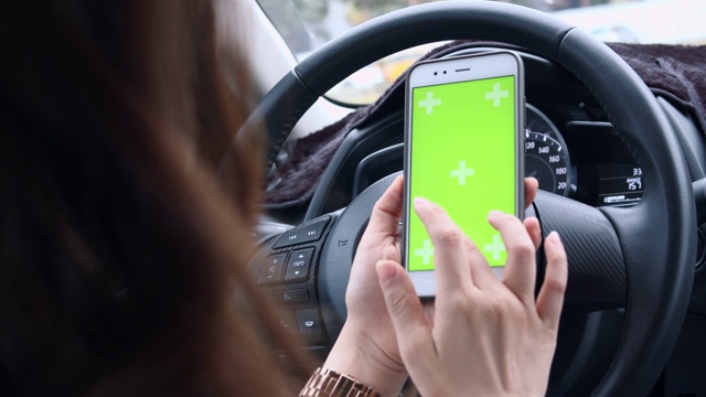 女人在路上开车并使用绿屏智能手机