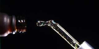 垂直镜头:在黑色背景和中心构图的慢镜头中，液滴从移液管落进瓶子里
