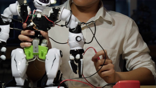 亚洲人工程师组装和测试机器人手臂反应在实验室。建筑师设计电路同步技术和协作开发机器人。