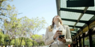 美女在等公交车的时候，一边在手机上看一些有趣的东西，一边喝着外卖咖啡