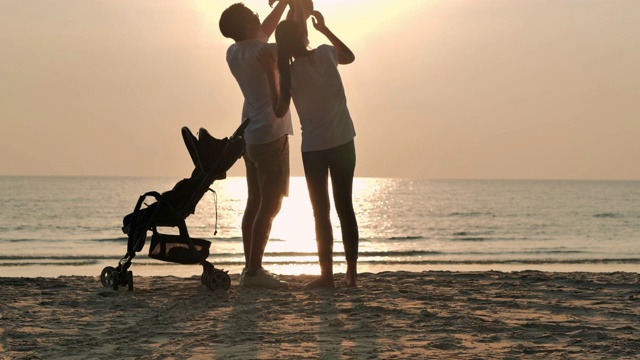 剪影快乐的父亲，母亲，婴儿儿子有乐趣沿海边的日落海浪在沙滩上。积极的父母和人在暑假带宝宝户外活动。幸福的家庭假期。家庭，生活方式，人，生命保险，假期-股票
