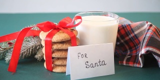 给圣诞老人的圣诞饼干。女人的手上放着一条短信，上面写着“送给圣诞老人”，旁边放着一杯牛奶、饼干、松枝和餐巾。