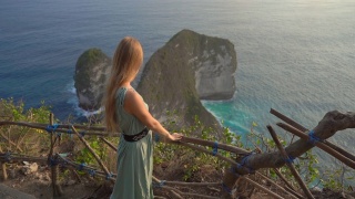 印尼努沙佩尼达克林金海滩，一名年轻的女游客正在参观所谓的霸王龙岩石。努沙佩尼达岛上著名的旅游景点。Slowmotion拍摄视频素材模板下载