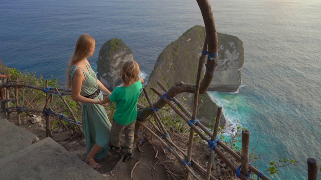一名年轻女子和她的小儿子在印度尼西亚努沙佩尼达克林金海滩参观所谓的暴龙岩石。努沙佩尼达岛上著名的旅游景点。Slowmotion拍摄