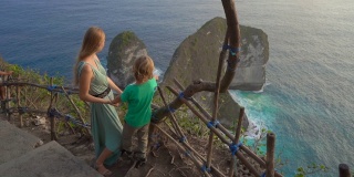 一名年轻女子和她的小儿子在印度尼西亚努沙佩尼达克林金海滩参观所谓的暴龙岩石。努沙佩尼达岛上著名的旅游景点。Slowmotion拍摄