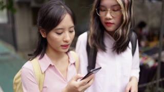 两个年轻的亚洲女孩走在街上用智能手机导航视频素材模板下载