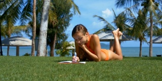 穿比基尼的女孩在绿草如茵的书上做笔记