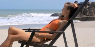 快乐的女人在沙滩上的木椅上放松