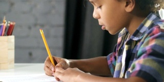 一个美国非洲男孩正坐在教室的桌子旁，在笔记本上做家庭作业