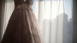 豪华现代婚纱挂在窗口。时尚的粉彩婚礼礼服蕾丝花的细节视频素材模板下载