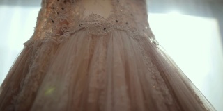 豪华现代婚纱挂在窗口。时尚的粉彩婚礼礼服蕾丝花的细节
