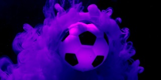 足球在惊人的空间背景。紫色和粉红色的墨水在水中在深蓝色的背景