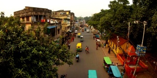 老加尔各答的夜晚街道，有汽车，行人，可以俯瞰摩托车，嘟嘟车，破旧的四层建筑，晾晒的衣服，绿树