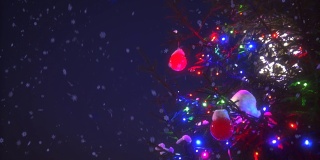 特写圣诞树的树枝与彩色的花环灯周围的雪花动画