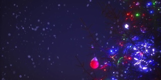 特写圣诞树的树枝与彩色的花环灯周围的雪花动画