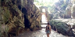 背对着光线，女孩穿过石拱离开洞穴