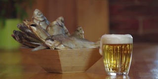 木质吧台上放着一杯清凉的淡啤酒。小吃,啤酒。装干鱼的木碗。