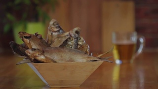 装干鱼的木碗。一只手拿起一杯啤酒。啤酒和鱼干。木质吧台上放着一杯清凉的淡啤酒。小吃,啤酒。视频素材模板下载