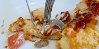 在餐馆里，年轻的亚洲妇女用刀把披萨切成小块，然后用叉子把它叼进嘴里。
