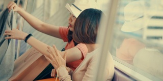 两个年轻的亚洲女人在地铁上展示她们在购物袋里买的新东西，慢镜头