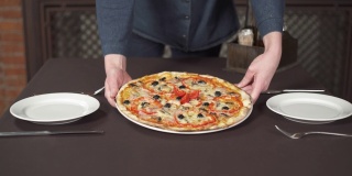 在café中，男性的手正在把一盘美味的披萨放到桌子上。传统的意大利食物，搭配奶酪和新鲜的番茄酱