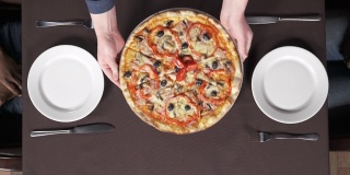 在披萨店，男性的双手正把一盘美味的披萨放到桌子上。传统意大利美食概念
