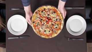 在披萨店，男性的双手正把一盘美味的披萨放到桌子上。传统意大利美食概念视频素材模板下载