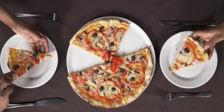 两只手拿起一片披萨，放进白盘子里。人们在吃意大利菜。饮食概念